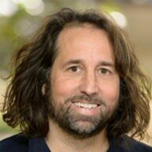 Headshot of Argonne researcher Andrew Siegel. He smiles and wears a black top. He stands in front of a nature backdrop.