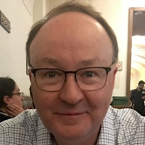 Photo of Los Alamos researcher David Daniel. He smiles, wears glasses, has a gray and black button up and sits at a table. 