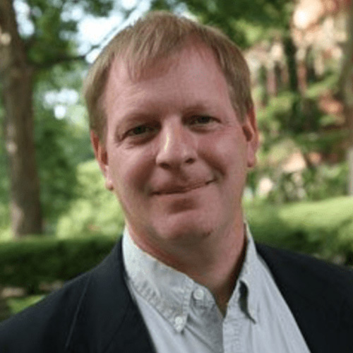 Headshot of Frederick National Laboratory for Cancer Research researcher Eric Stahlberg. He smiles and wears a light colored button up with blazer. He stands in front of a nature background.