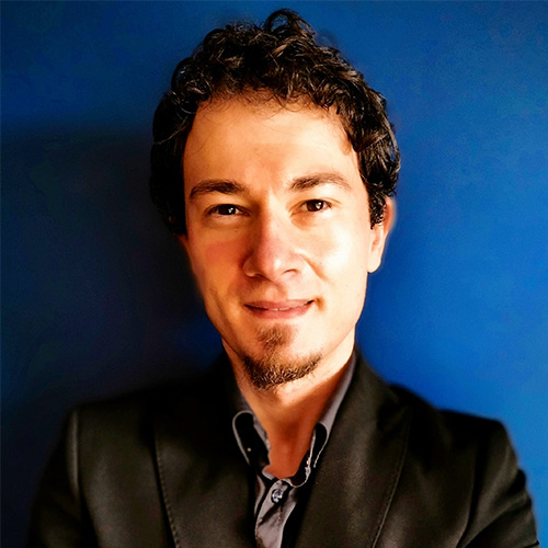 Headshot of Ames researcher Giuseppe Barca. He smiles and wears a black suite with gray button up. He stands in front of a blue backdrop.