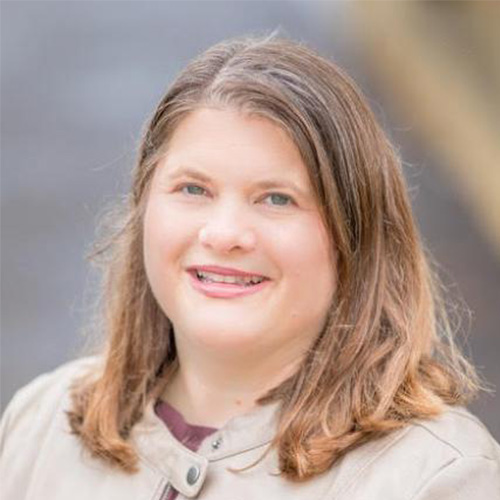 Headshot of SLAC researcher Jana Thayer. She smiles and wears a red blouse with brown jacket. She stands in front of a blurred background.