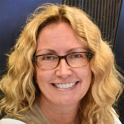 Headshot of Brookhaven researcher Kerstin Kleese van Dam. She smiles, wears a cream colored blazer with matching blouse. She stands against a navy and black background. 