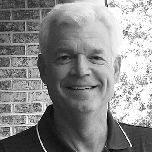 Headshot of Oak Ridge researcher Doug Kothe. His photo is in black and white. He smiles and stands against a brick wall.