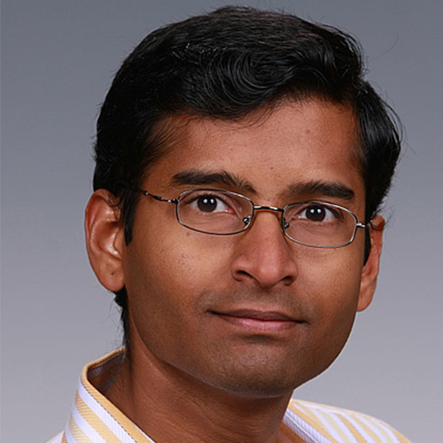 Headshot of Pacific Northwest researcher Sriram Krishnamoorthy. He smiles, has glasses, and stands against a light grey background. 