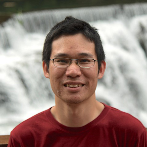 Headshot of SLAC National Accelerator researcher Yee Ting Li. He smiles and wears glasses. He stands in front of a waterfall. 