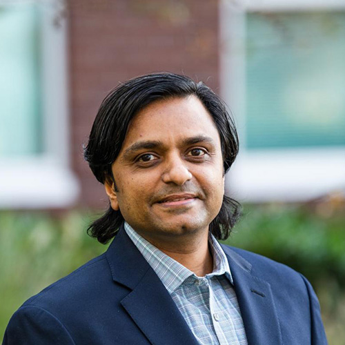 Headshot of Pacific Northwest researcher Mahantesh Halappanavar. He smiles and wears a light colored button up with a navy blazer. He stands in front of a blurred nature scene.