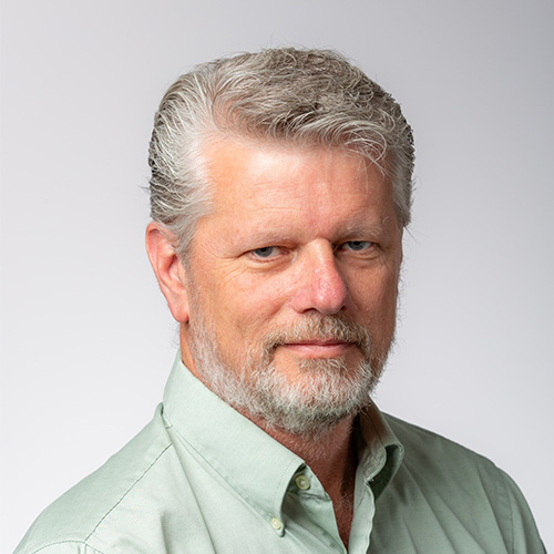 Headshot of National Renewable Energy researcher Marc Day. He smiles and wears a light green colored button up. He stands in front of a white backdrop.