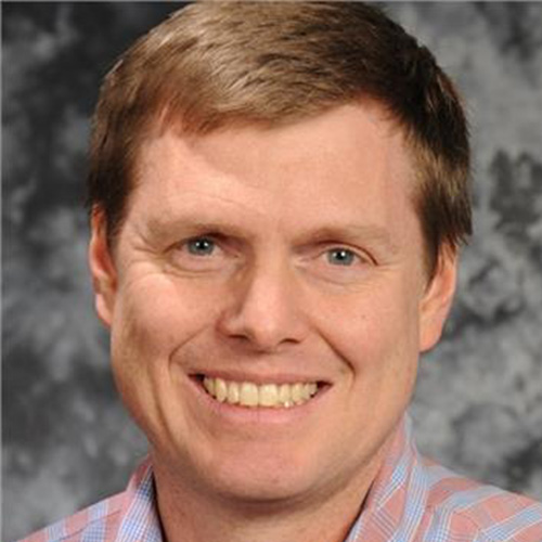 Headshot of Idaho National researcher Matthew Anderson. He smiles and wears a blue and green flannel. He stands in front of a gray backdrop.