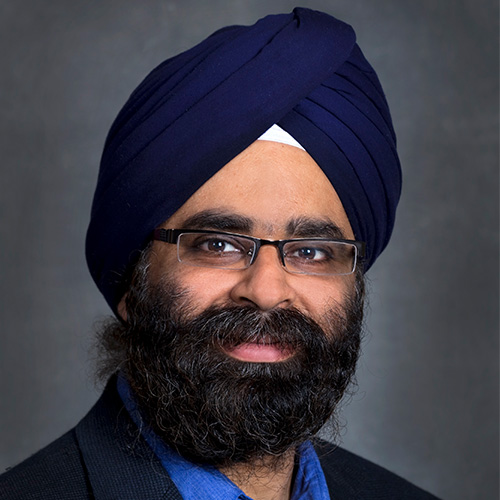 Headshot of Lawrence Berkeley researcher Inder Monga. He smiles, wears a blue button up with black blazer, has a navy colored dastar, and stands against a dark grey background. 