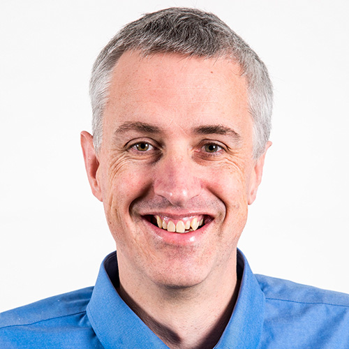 Headshot of Lawrence Berkeley researcher Nick Wright. He smiles, wears a blue button up, and stands against a white background. 