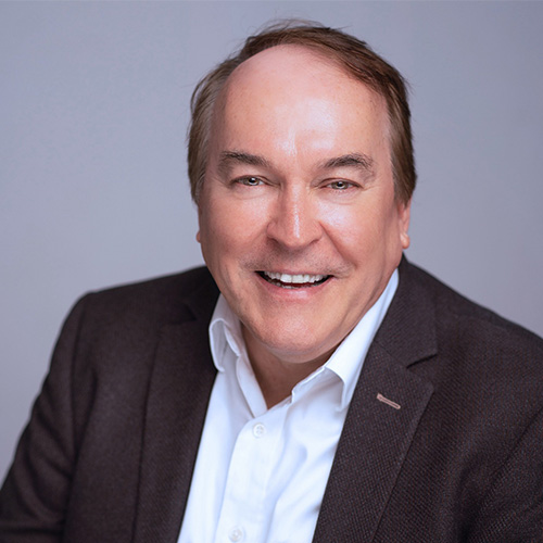 Headshot of University College London researcher Peter Coveney. He smiles and wears a light colored button up with blazer. He stands in front of a gray backdrop.