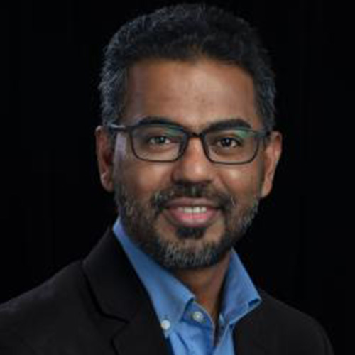 Headshot of Oak Ridge researcher Prasanna Balaprakash. He smiles and wears a blue button up with black blazer. He has glasses. He stands in front of a black back drop.