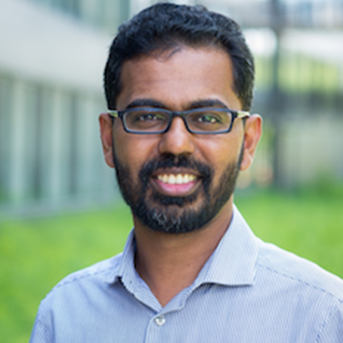 Photo of Argonne researcher Prasanna Balaprakash. He smiles and wears glasses. He wears a light blue button up and stands against a nature backdrop.