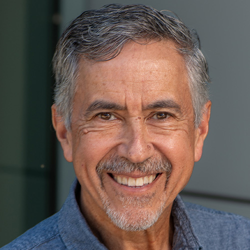 Headshot of National Energy Research Scientific Computing Center researcher Richard Gerber. He smiles and wears a blue button up. He stands in front of a gray background.