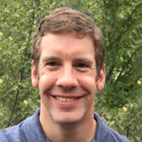 Headshot of Lawrence Livermore researcher Todd Gamblin. He smiles and wears a light blue button up. He stands in front of a tree.