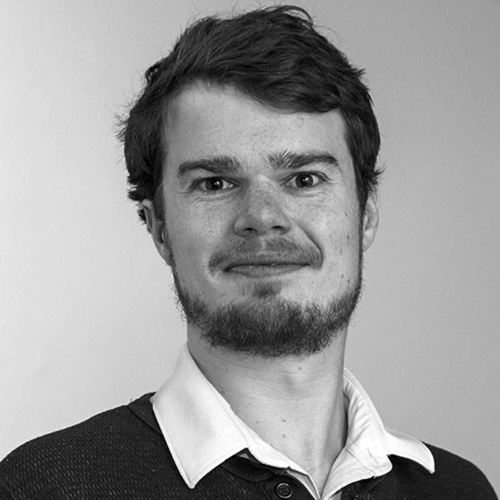 Headshot of Princeton Plasma Physics researcher Andrew Tasman. His headshot is in black and white. He smiles and wears a button up shirt. He stands in front of a backdrop.