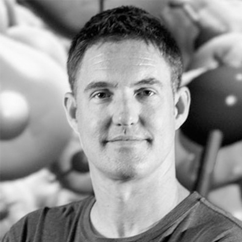 Headshot of Lawrence Livermore researcher Erik Draeger. His headshot is in black and white. He smiles and stands in front of an abstract background.